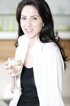 Beautiful young woman enjoying a glass of wine in her kitchen.