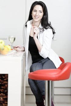 Beautiful young woman enjoying a glass of wine in her kitchen, while preparing food.
