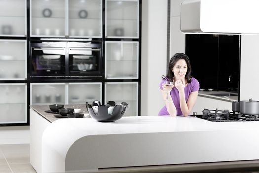 Attractive young woman in a dinner dress holding a glass of wine in her kitchen.