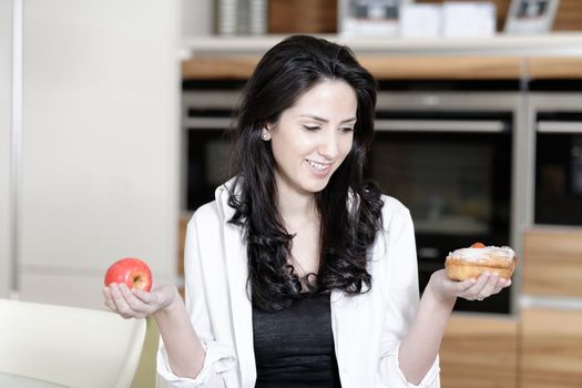 Attractive young woman choosing between a sticky cake or fresh fruit.