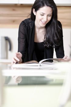 Beautiful young woman reading from a recipe book in her kitchen