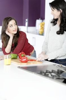 Two attractive young women preparing food in a white kitchen while talking.