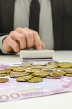 Close up of businessman working on calculator with pile of money on his desk. Focus on the money.