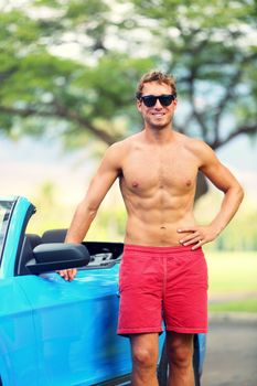 Handsome man with sports car. Well built fit young male model standing shirtless leaning on the door of a blue sports car smiling at the camera.