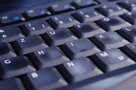 A black keyboard illuminated by the computer screen. Selective Focus.