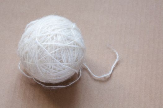 Ball of white wool yarn on cardboard background