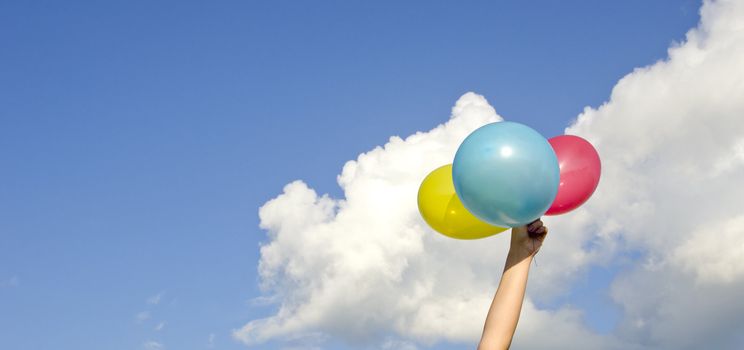 girls hand holding three colorful balloons and cloudy sky