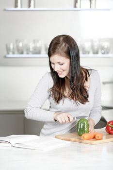 Beautiful young woman reading from a cookery book while cooking in her kitchen.