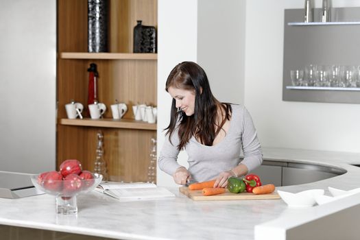 Beautiful young woman reading from a cookery book while cooking in her kitchen.