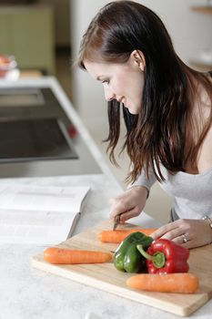 Beautiful young woman reading from a cookery book while cooking in her kitchen.