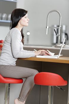 Attractive young woman in her elegant kitchen taking a break with her laptop