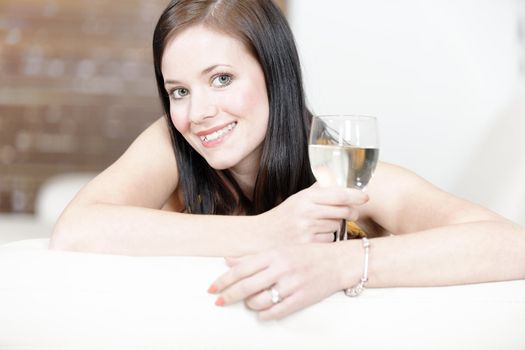 Attractive young woman lying on her sofa enjoying a glass of wine.