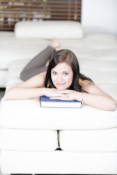 Attractive young woman lying on her sofa with a book.