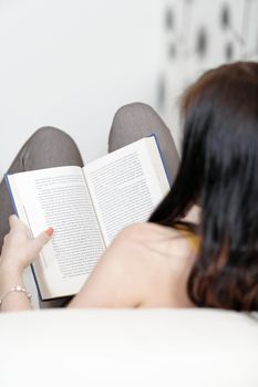 Attractive young woman lying on her sofa with a book.