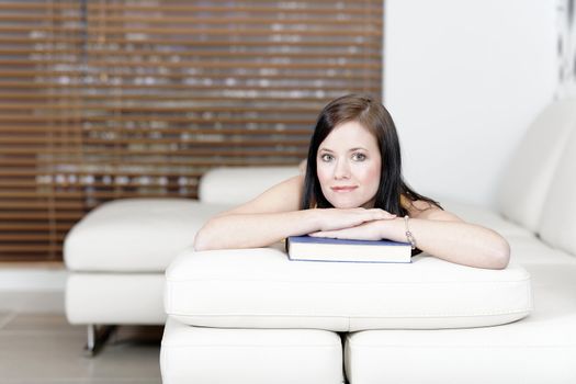 Attractive young woman lying on her sofa with a book.