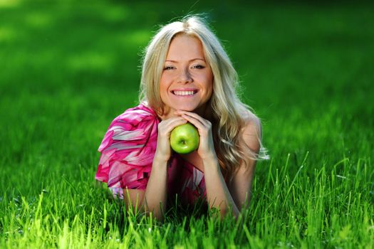 blonde holding an apple in his hand lying on green grass