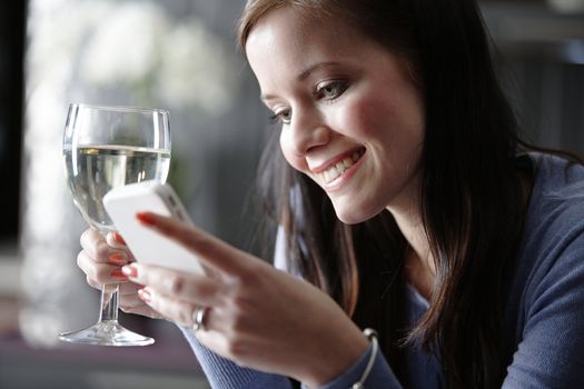 Attractive young woman enjoying a glass of wine in her kitchen while chatting on the phone.