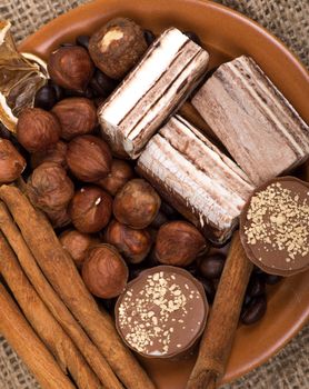 Sweets, cinnamon, nuts and coffee beans on a saucer, on burlap background.