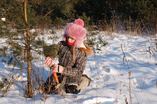 little girl in winter forest puts carrots on tree so wild animal can eat it