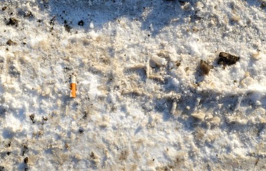 Winter snow path closeup background and cigarette butt thrown on ground.