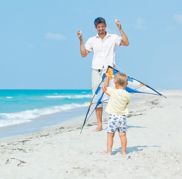 Little cute boy playing his father with a colorful kite on the tropical beach.