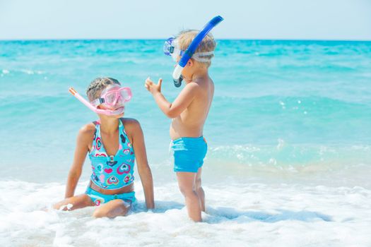 Smiling Happy brother and sister posing on a beach wearing snorkeling equipment. In the background the sea