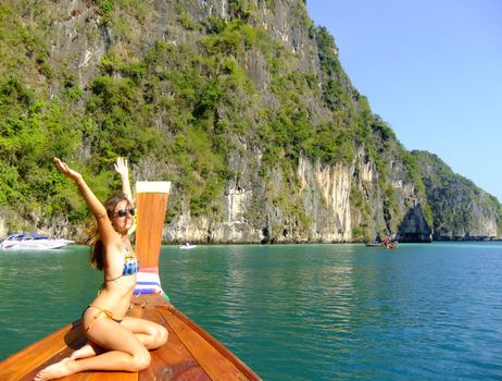 Young woman in bikini sitting on a stern of longtail boat, Phi Phi Lei island, Thailand