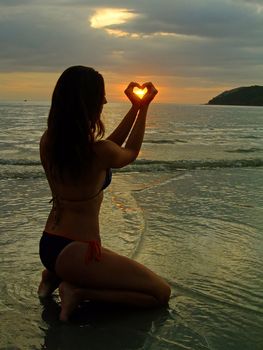 Silhouette of young woman making heart shape with her hands at sunset