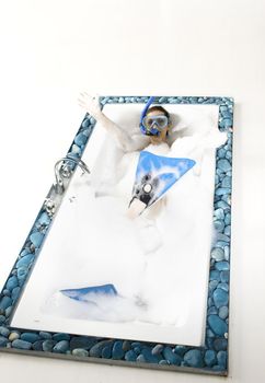Young woman enjoying the bath-foam in the bathtub with blue rubber scuba tools