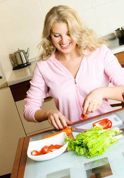 beautiful young blond woman at home in the kitchen making salad
