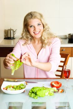 beautiful young blond woman at home in the kitchen making salad