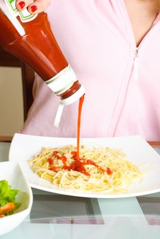 woman pouring tomato ketchup into the plate with spaghetti