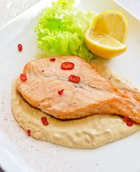 Grilled salmon steak with greens, lemon, sauce and pepper chile