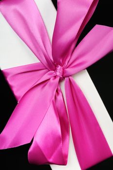 Gift box with a big pink bow close up. On a dark background.