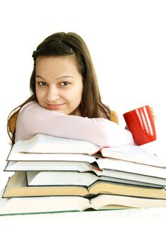 happy caucasian teenage girl sitting at the desk with stack of opened books and tea cup