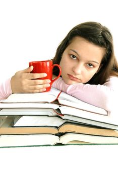 caucasian teenage girl sitting at the desk with stack of opened books and tea cup