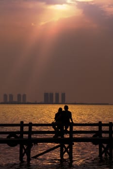 Silhouette of couple enjoying romantic sunset on the bridge at the sea.