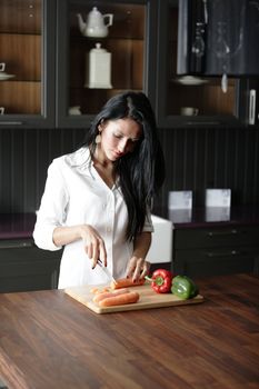 Attractive young woman chopping up fresh vegetables and peppers in her kitchen.