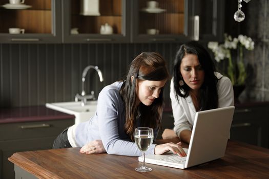 Two attractive friends looking at recipes on a laptop in their kitchen.