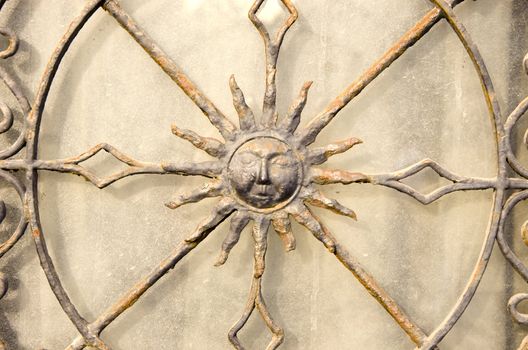 Closeup of decorative metal gate. Sun is shown in middle.