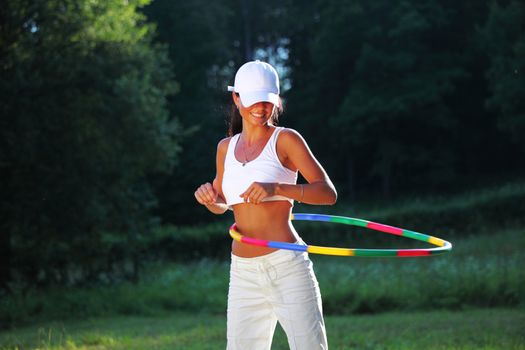 woman rotates hula hoop on nature background