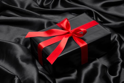 Black gift box with red satin ribbon and bow, over black satin