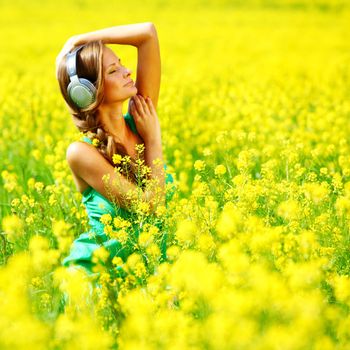  Young woman with headphones listening to music on oilseed flowering field