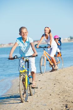 Cute girl with her mother and brother ride bikes along the beach. Focus on girl. Vertical view