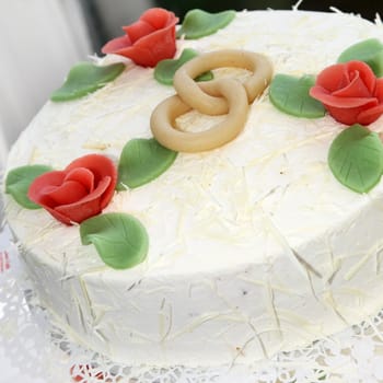 Two-layered wedding cake decorated with orangey red rose buds and intertwined wedding rings