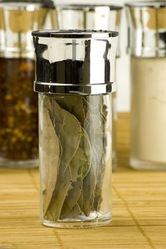 dry bay leaves in a glass jar on different spices background over wooden mat