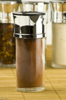 chili powder in a glass jar on different spices background over wooden mat