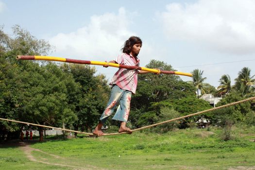 A young poor trapeze girl balances on her rope and does her tricks to make a living, in India.