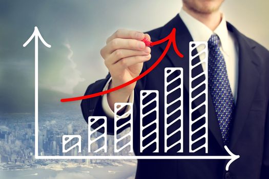 Businessman drawing a rising arrow over a bar graph above the city