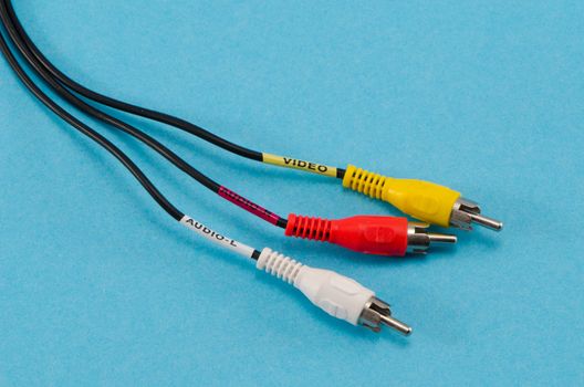 closeup of colorful tulip video audio tv cable wires on blue background. red yellow and white connectors plugs.